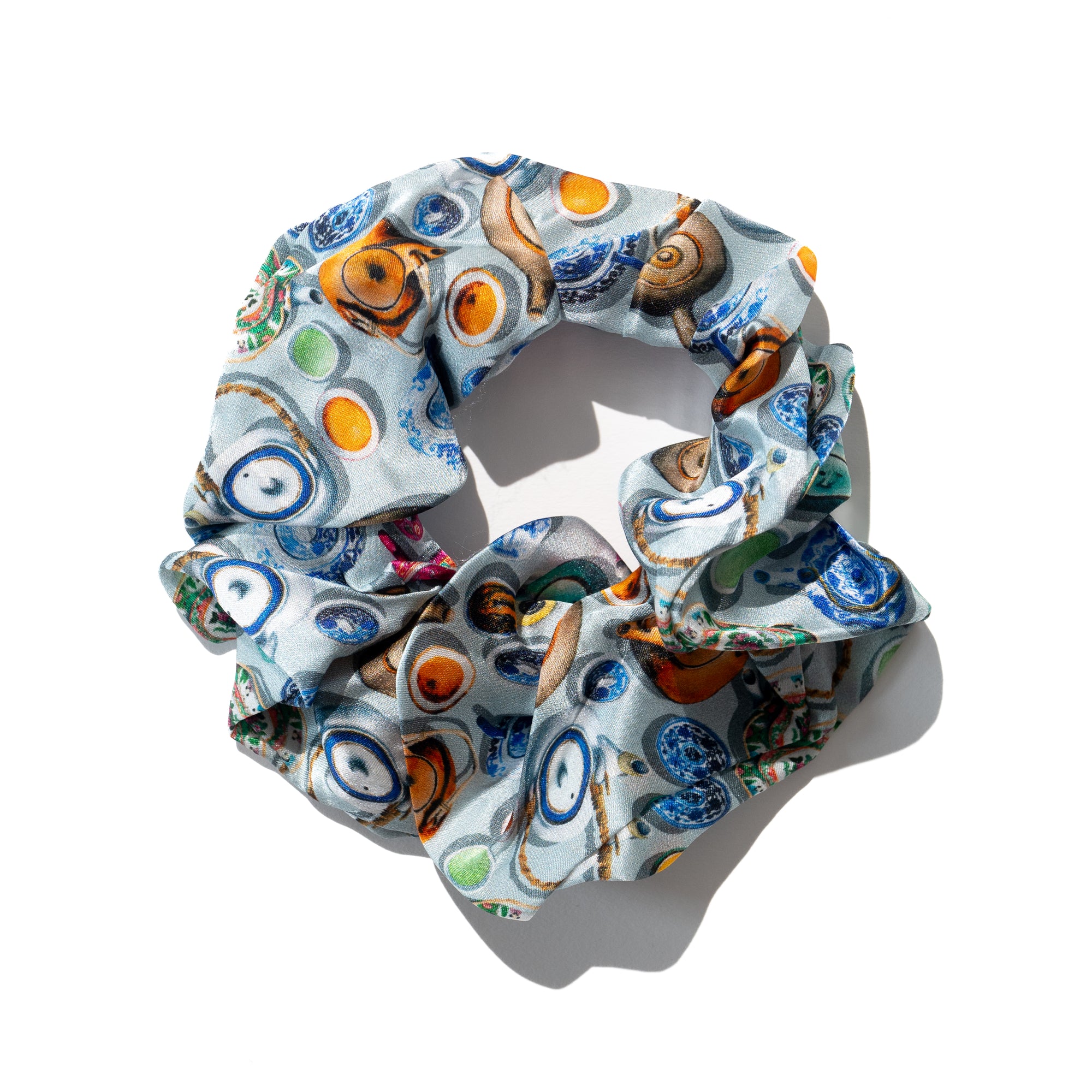A multicolored silk scrunchie with a pattern of chinese teapots and cups displayed on a light background.
