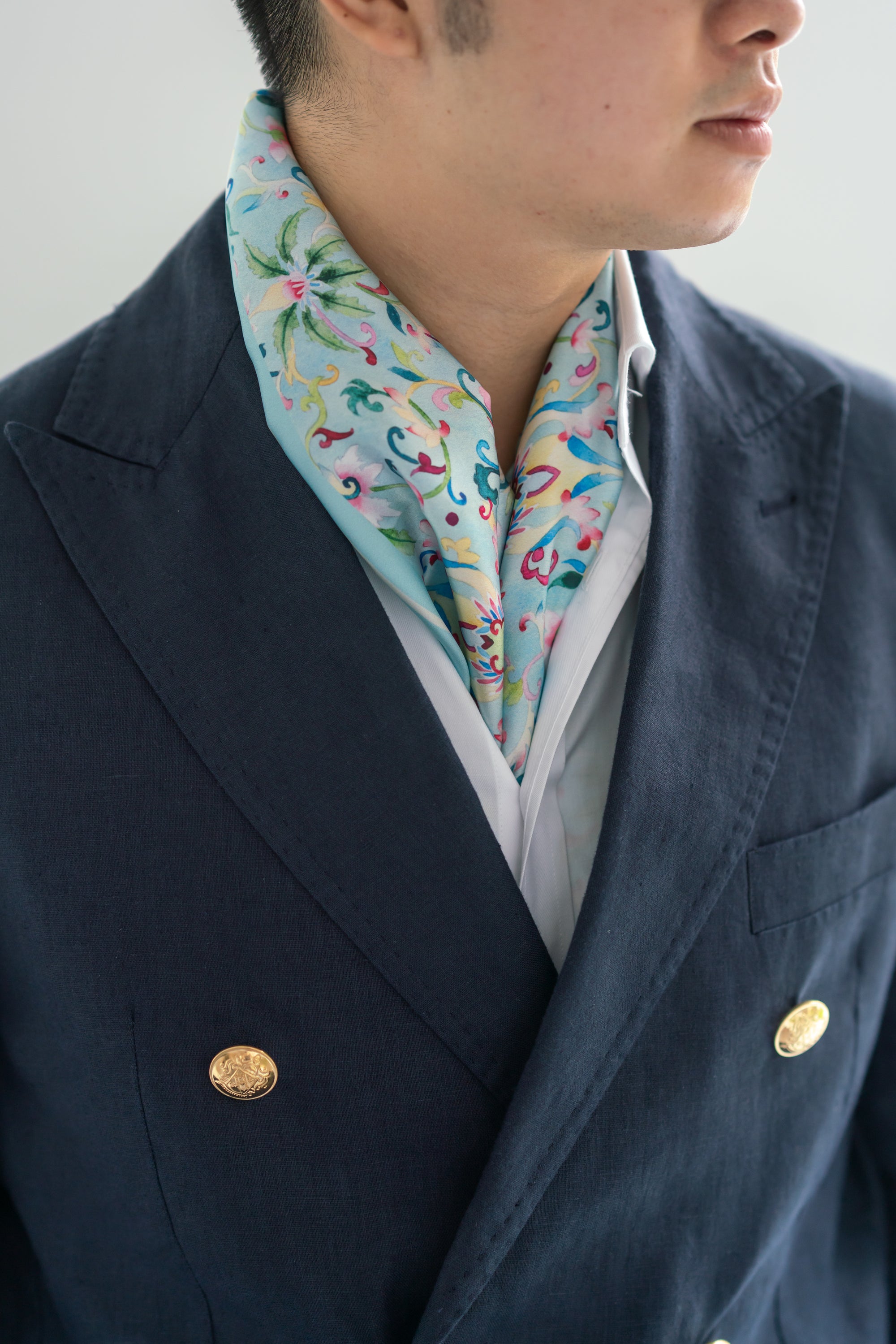 A person wearing a navy blazer and a white shirt with a Chinese floral silk scarf in their neck area.