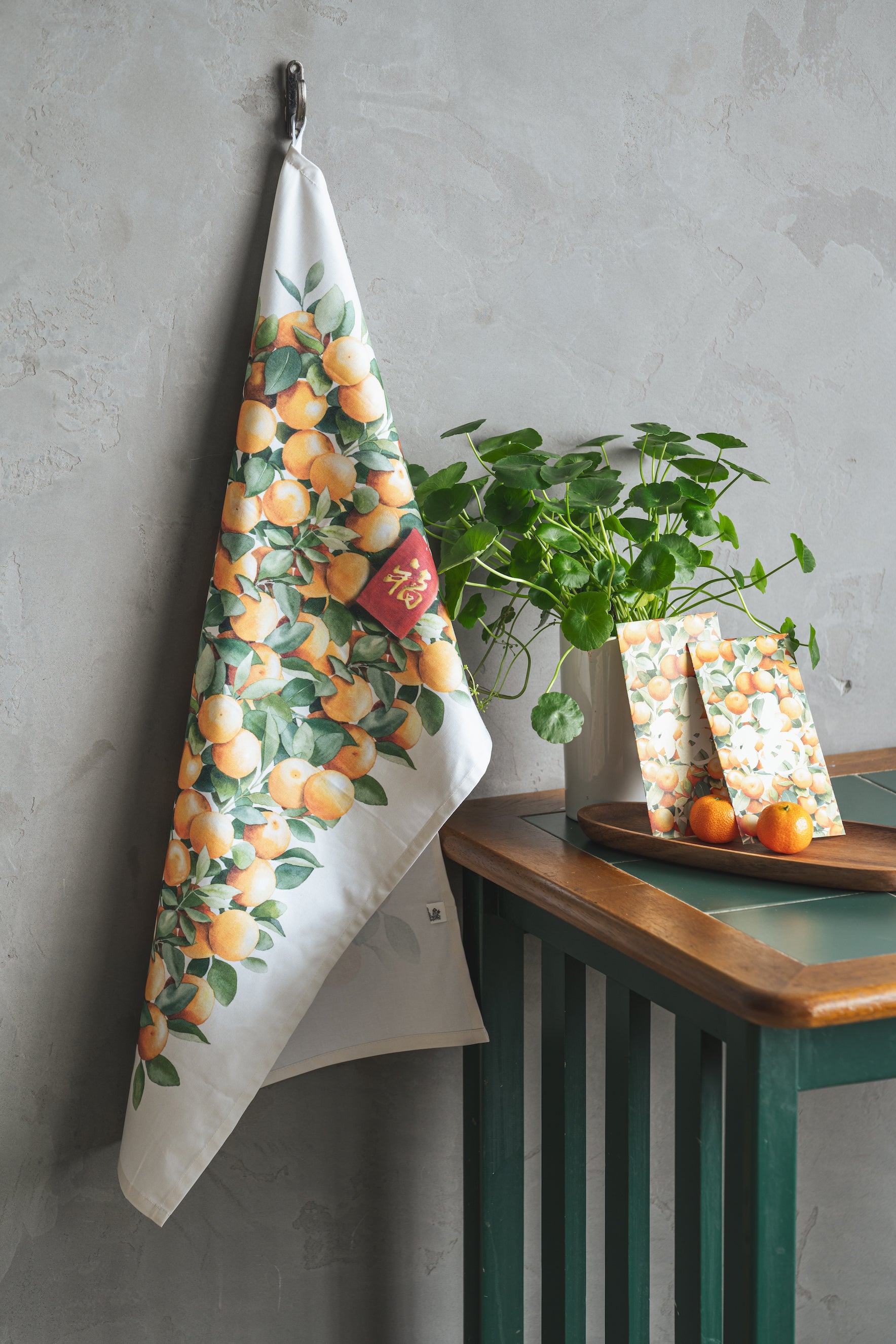 Display of Orange tree tea towel alongside a table, oranges and red packets
