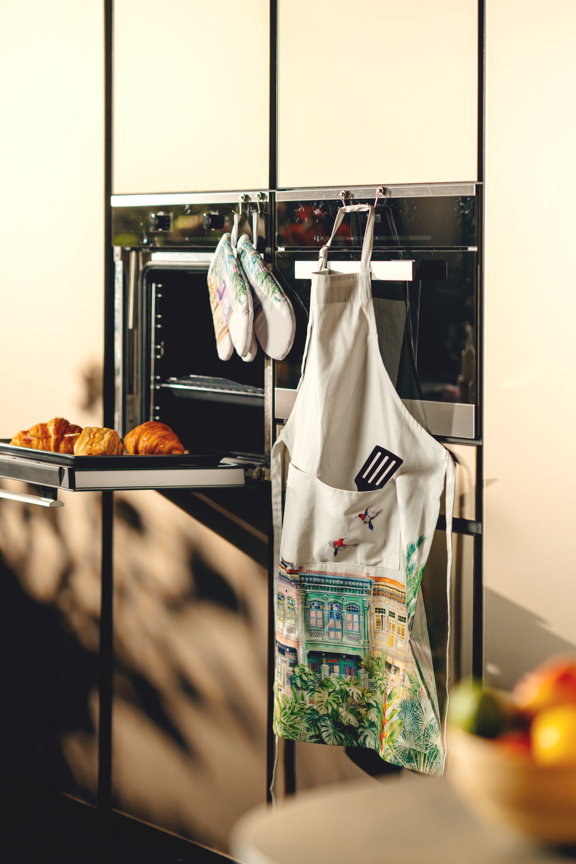 Aprons hanging on a rack with a tray of pastries and fruits in the foreground.