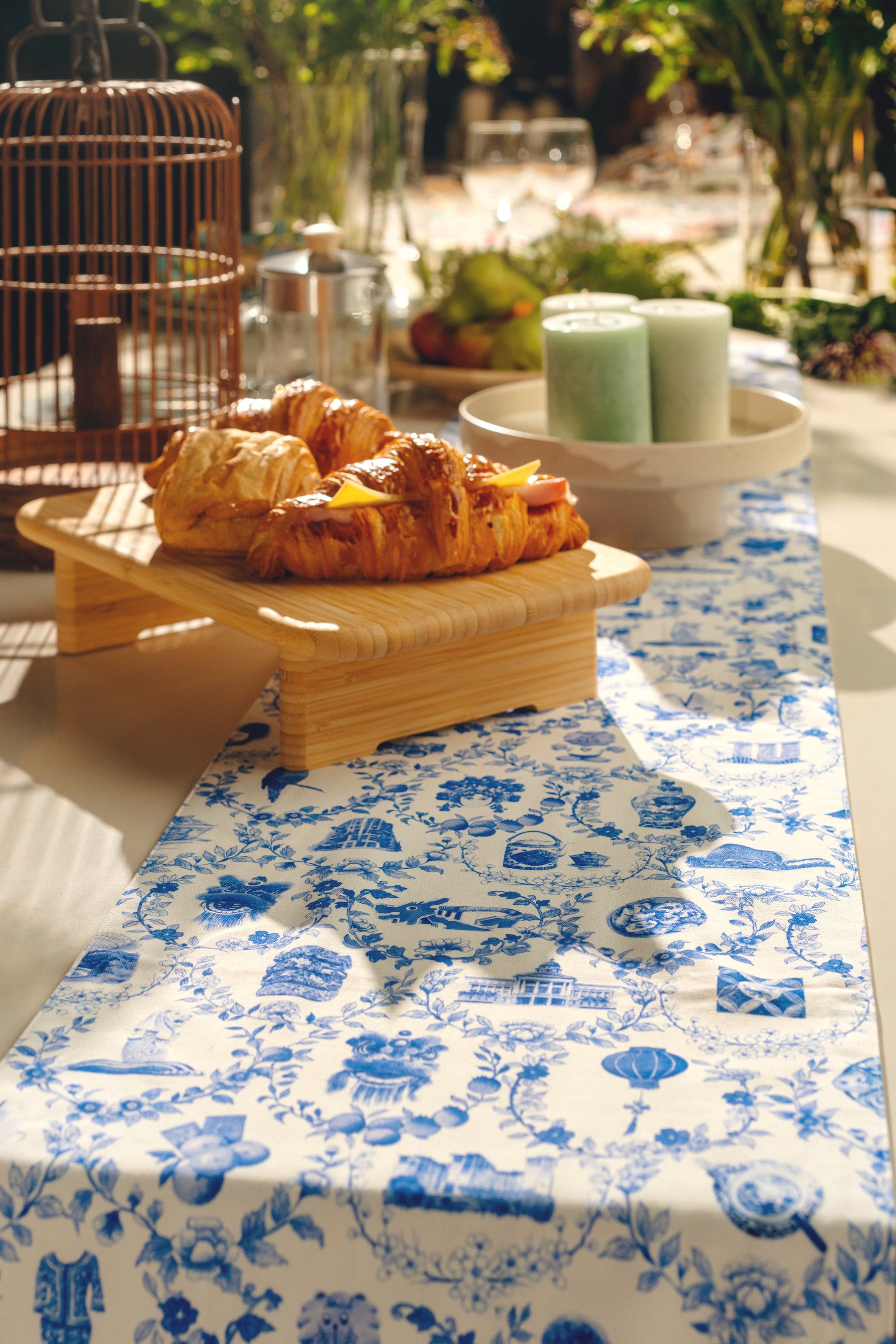 Pastries on a wooden tray and candles on a candle holder with a blue and white patterned tablecloth.