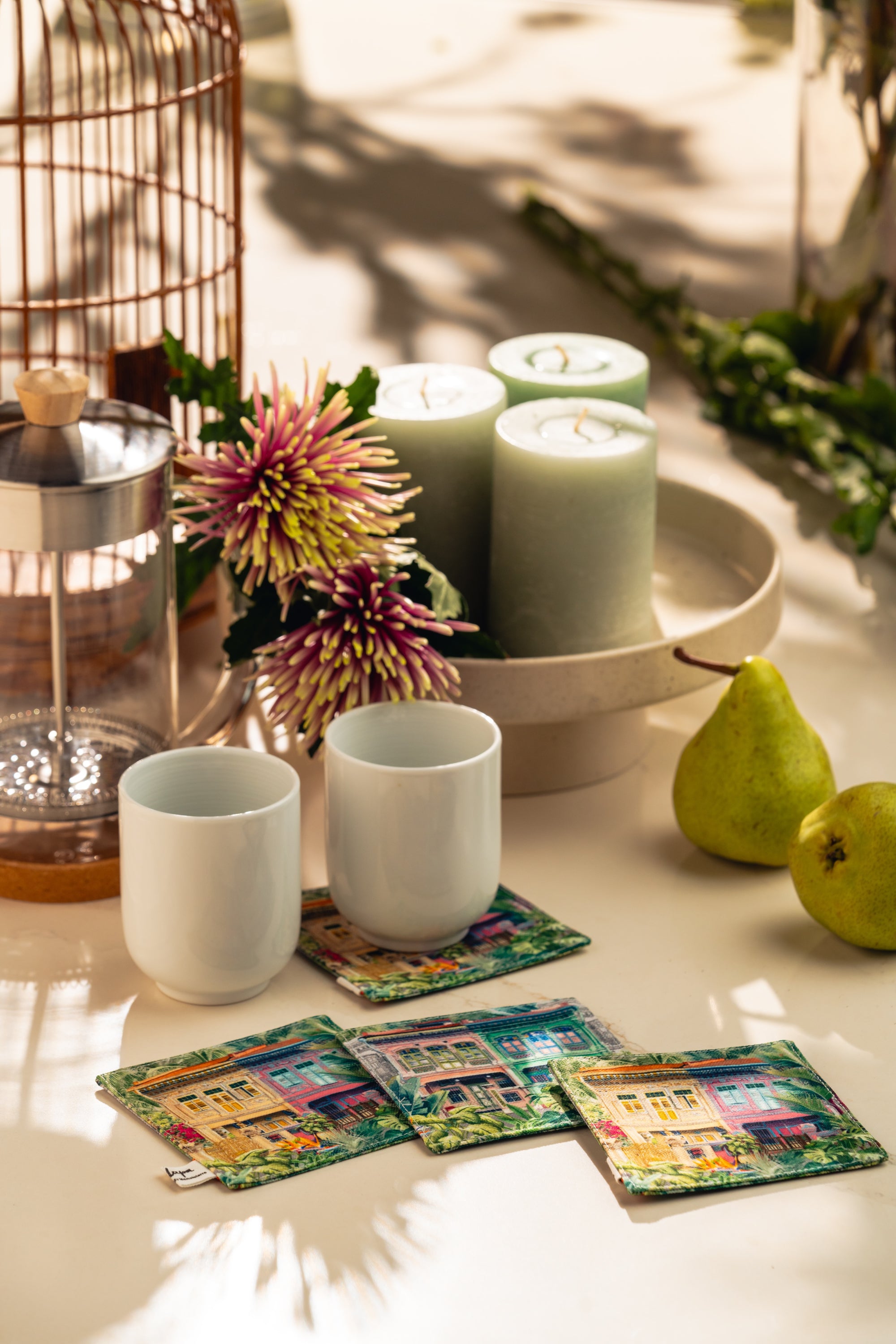 Candle holder with candles, cups, and colorful coasters on a table with greenery.