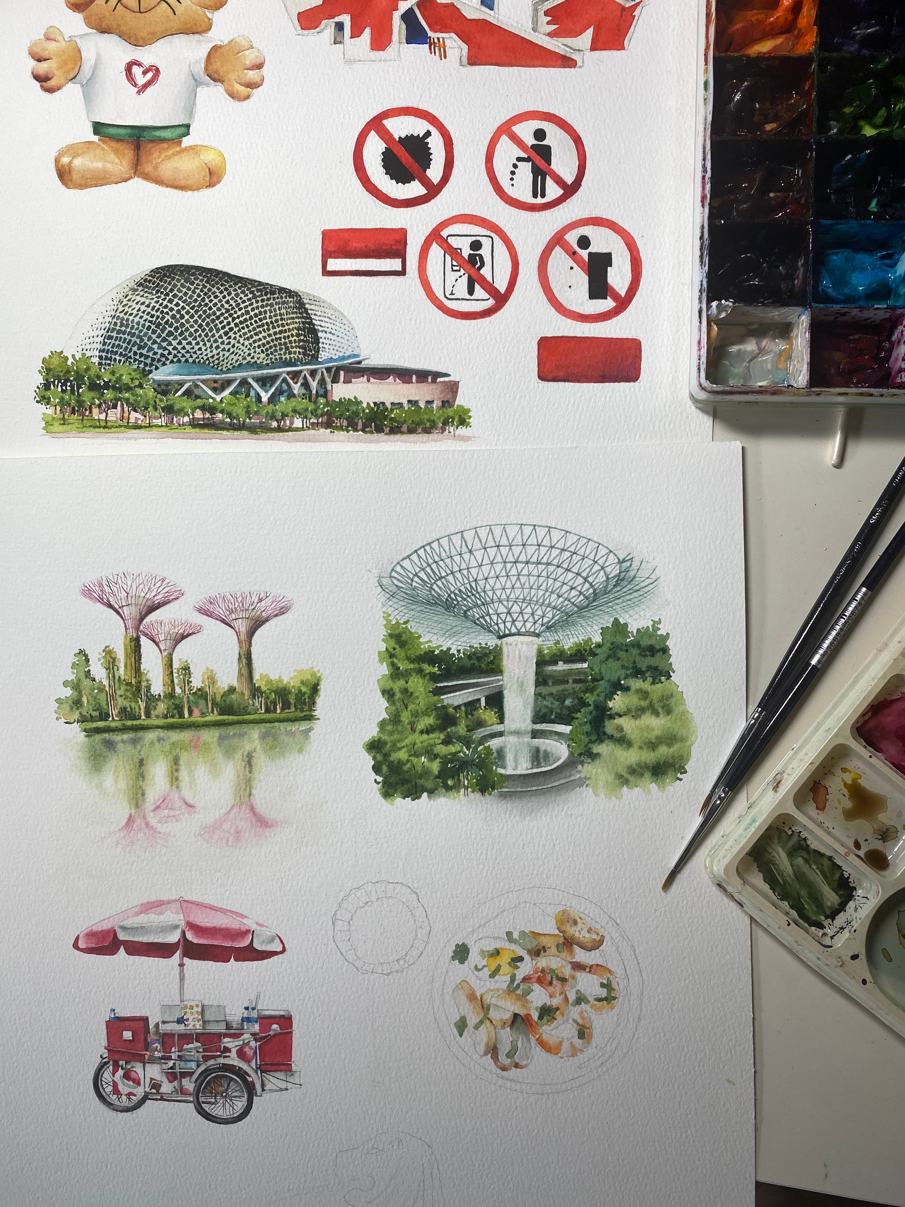 Artistic illustrations of Singapore landmarks on a watercolor paper with a watercolor set above.