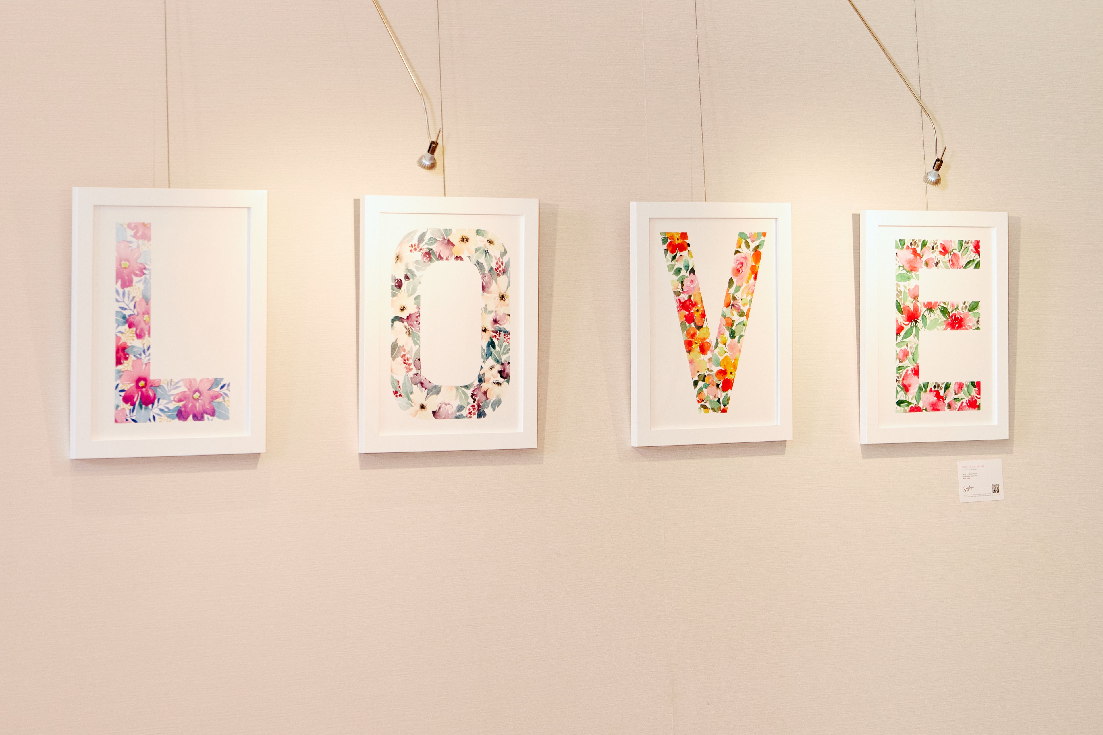 Four framed floral letters spelling 'LOVE' on a beige wall.