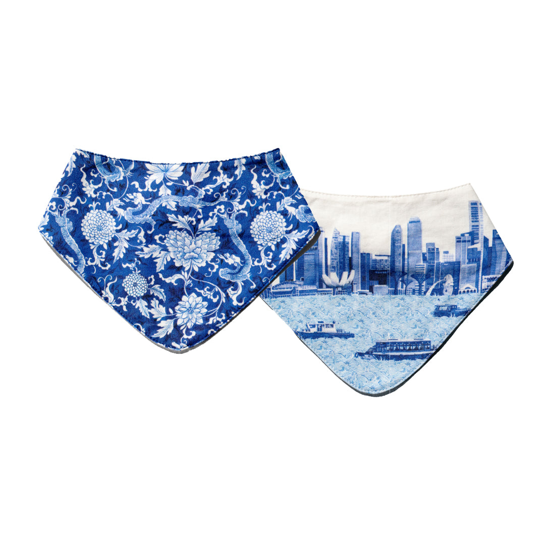 Singlapa Two baby bibs, one with a blue floral dragon pattern and the other with a white cityscape design.