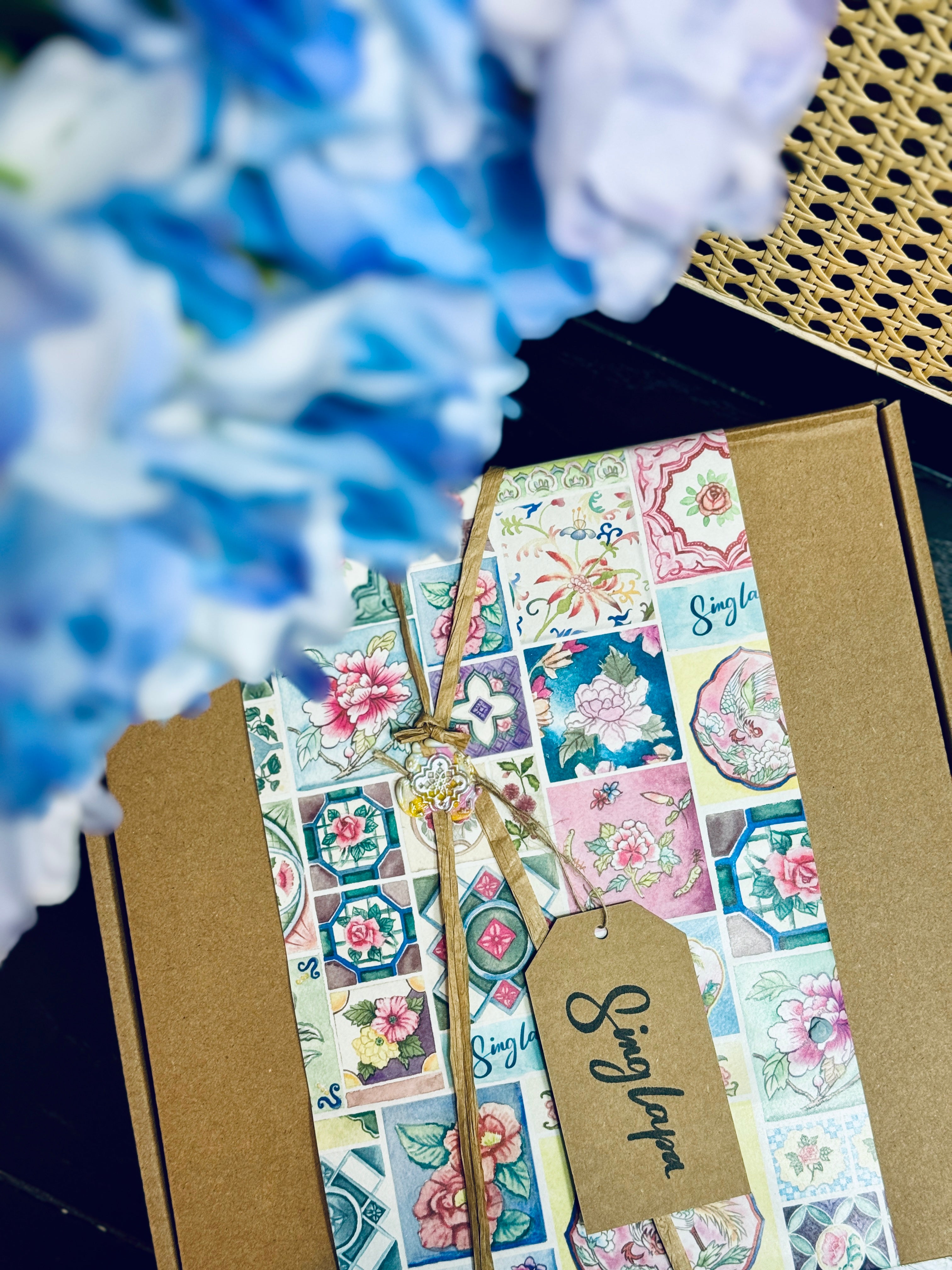 Decorative paper strips with floral designs and a tag on a brown box with blue flowers in the background.