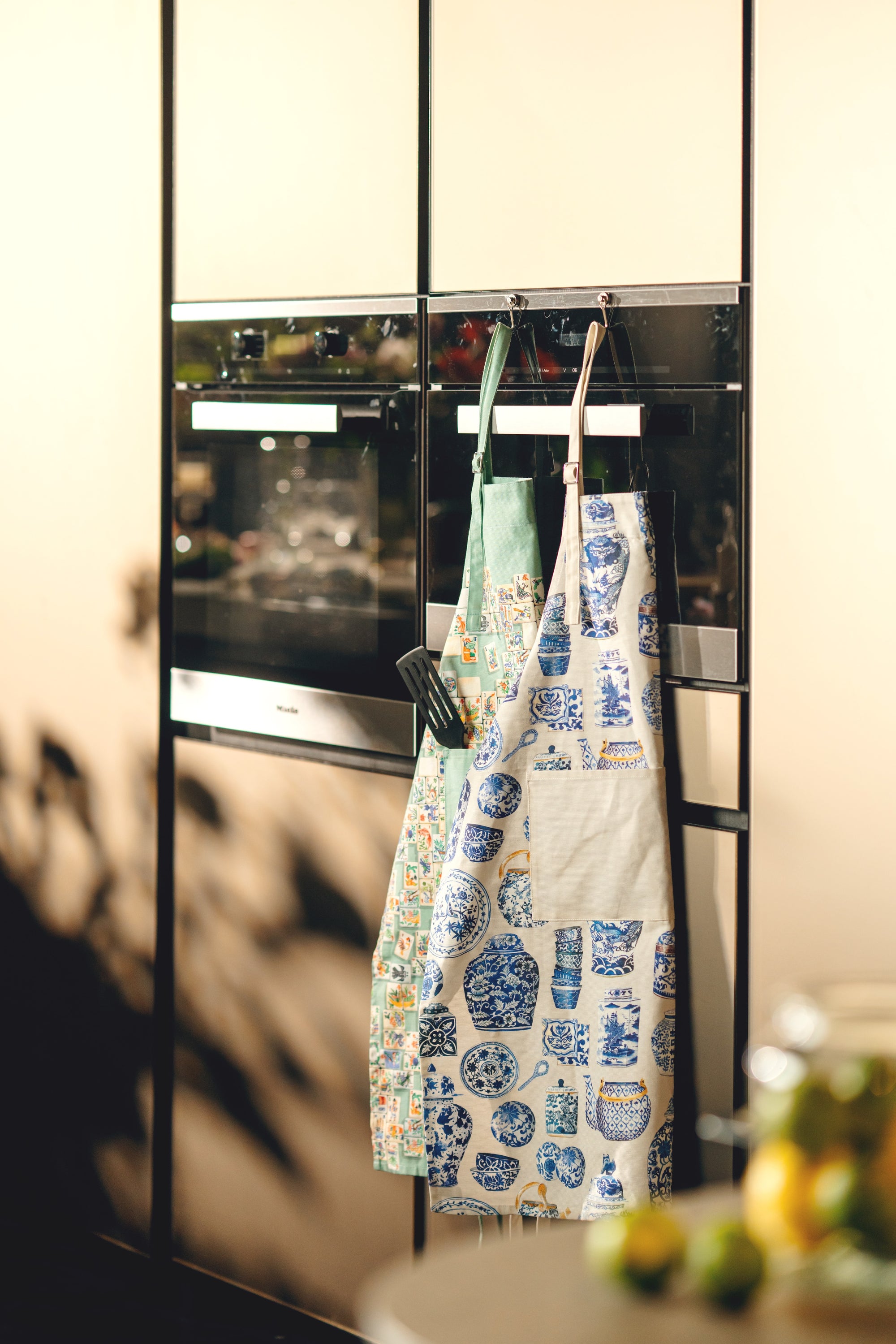 Two aprons hanging on a rack in a kitchen setting with a blurred background