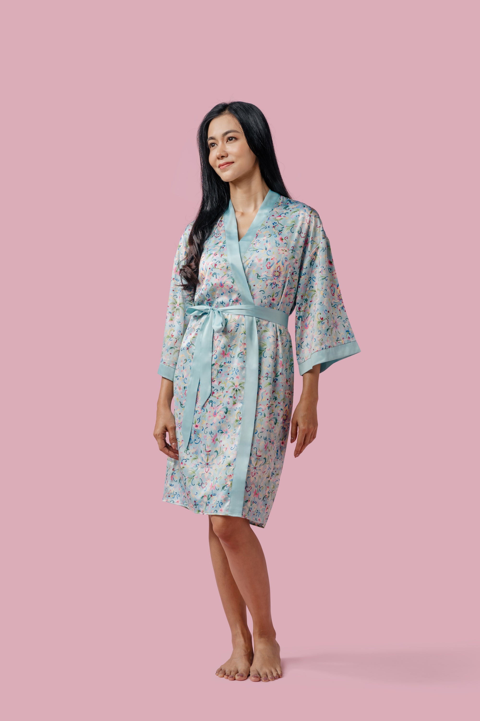 Woman wearing a blue silky kimono on a pink background.