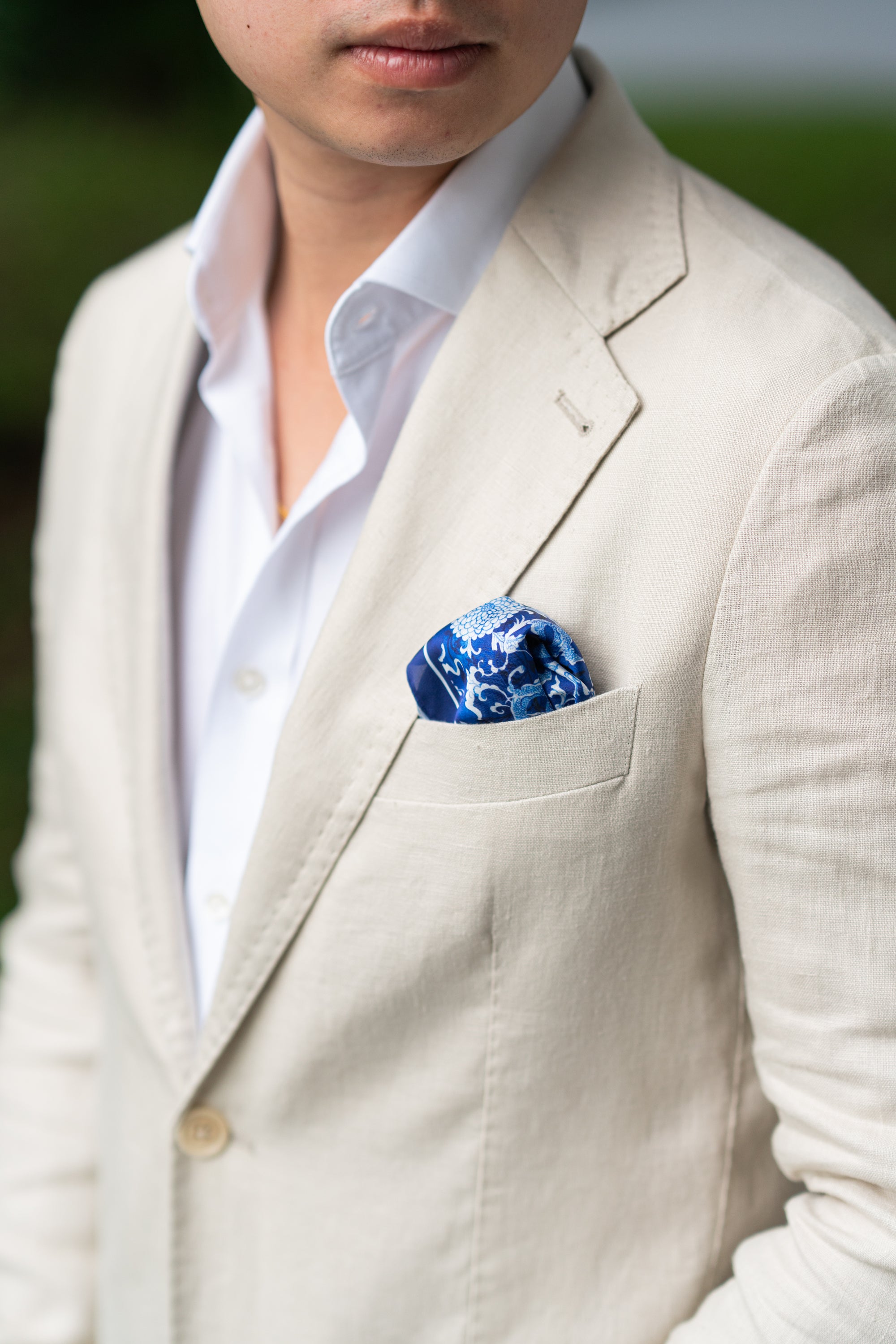 Man wearing a beige suit with a blue dragon pocket square.