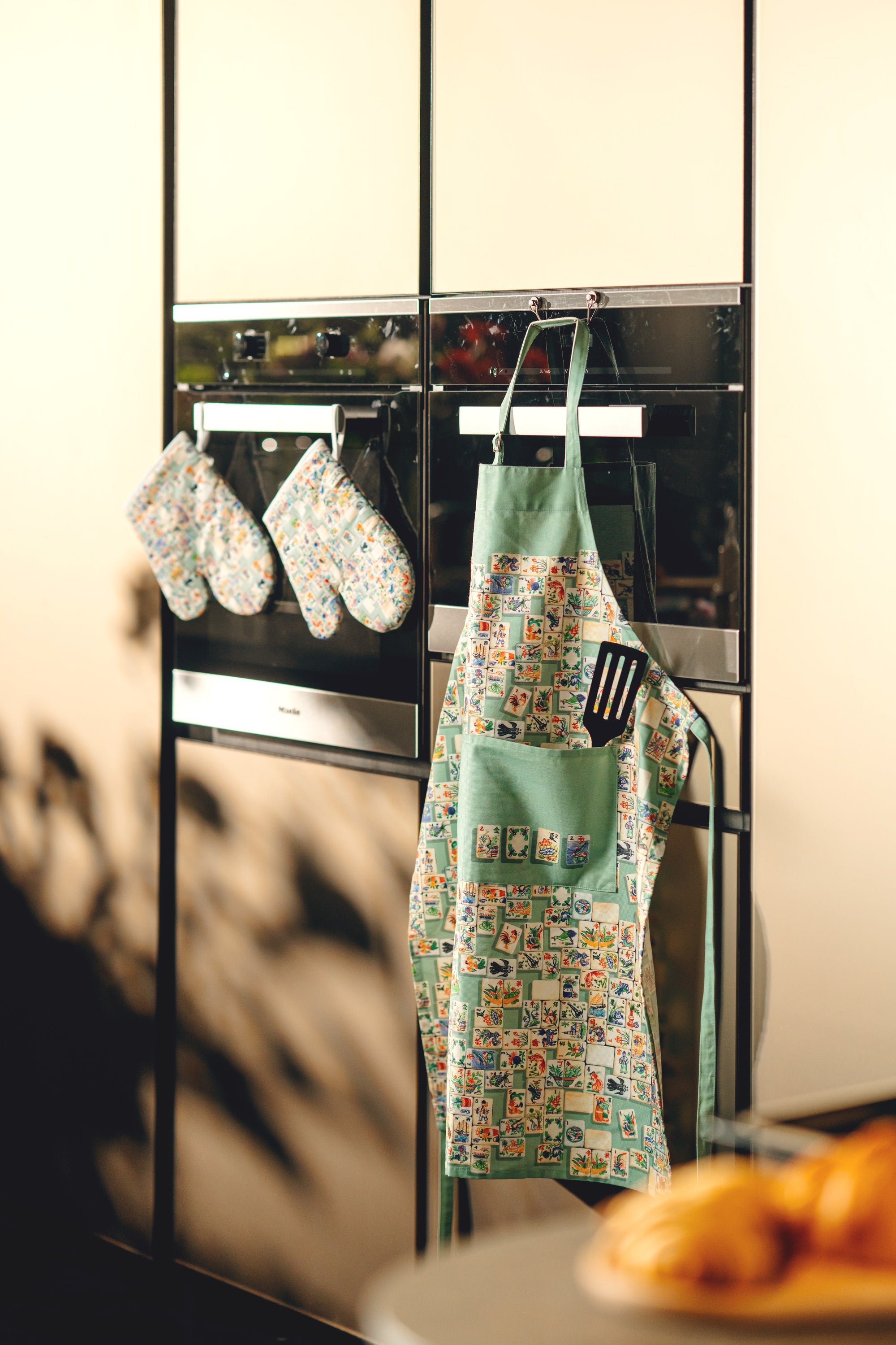 Green apron with colorful patterns hanging on a kitchen oven door.