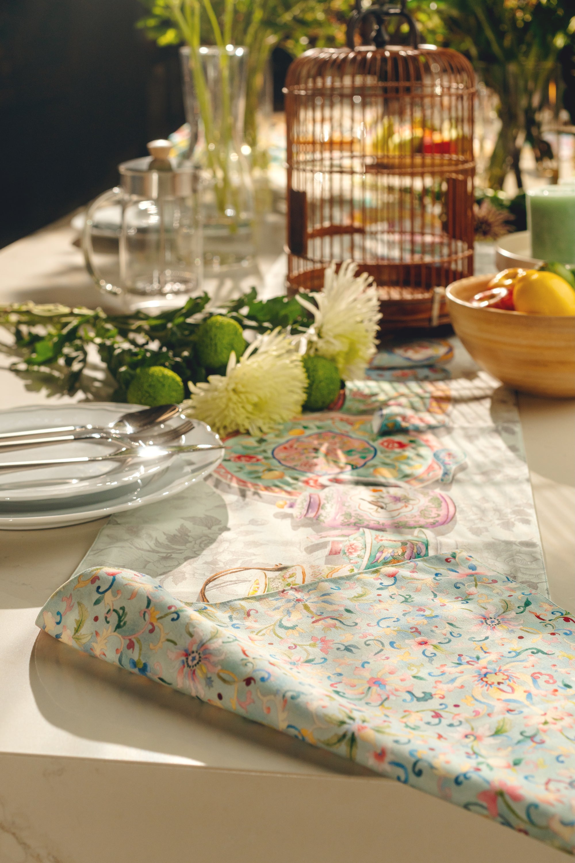 Decorative table setting with floral table runner, plates, and cutlery on a white table.