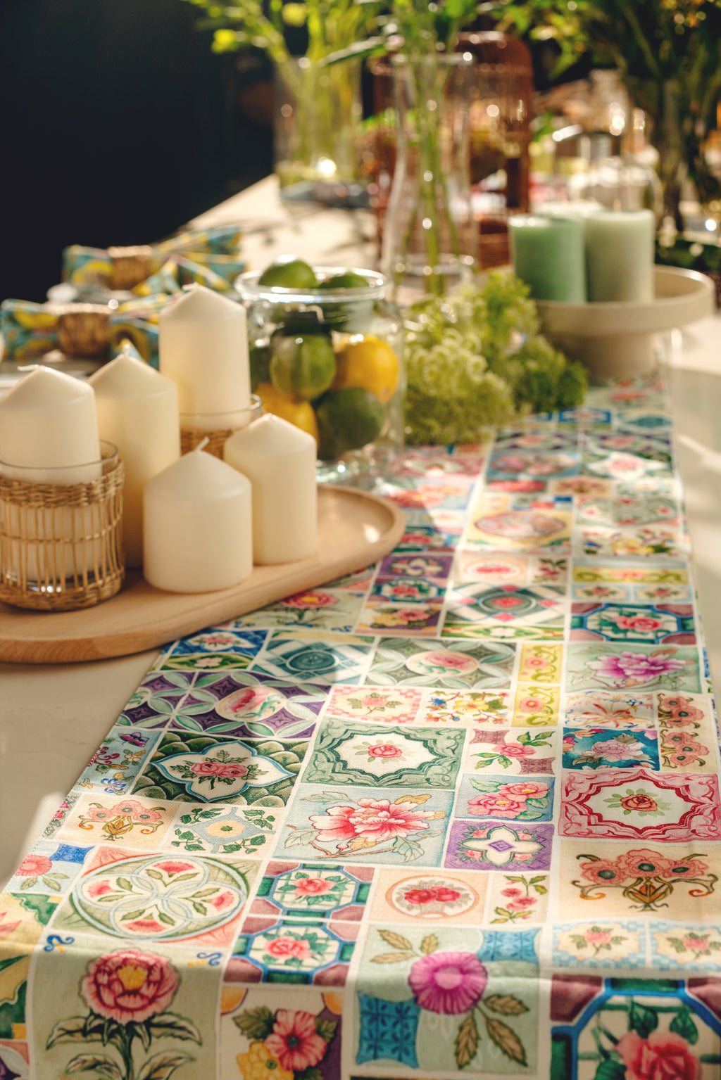 Decorative table setting with a floral patterned tablecloth, candles, and fruit bowl.