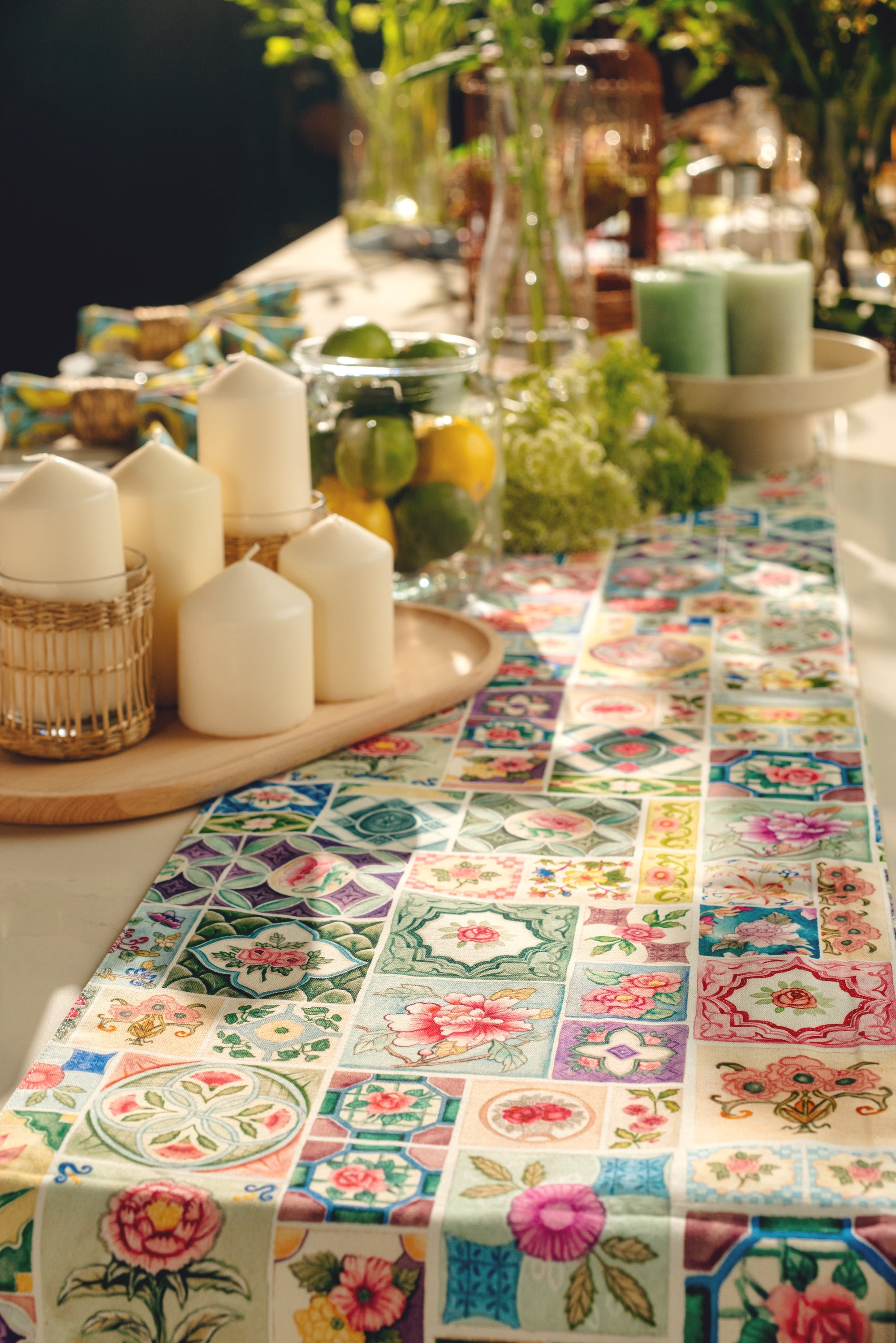 Decorative table setting with a floral patterned tablecloth, candles, and fruit bowl.