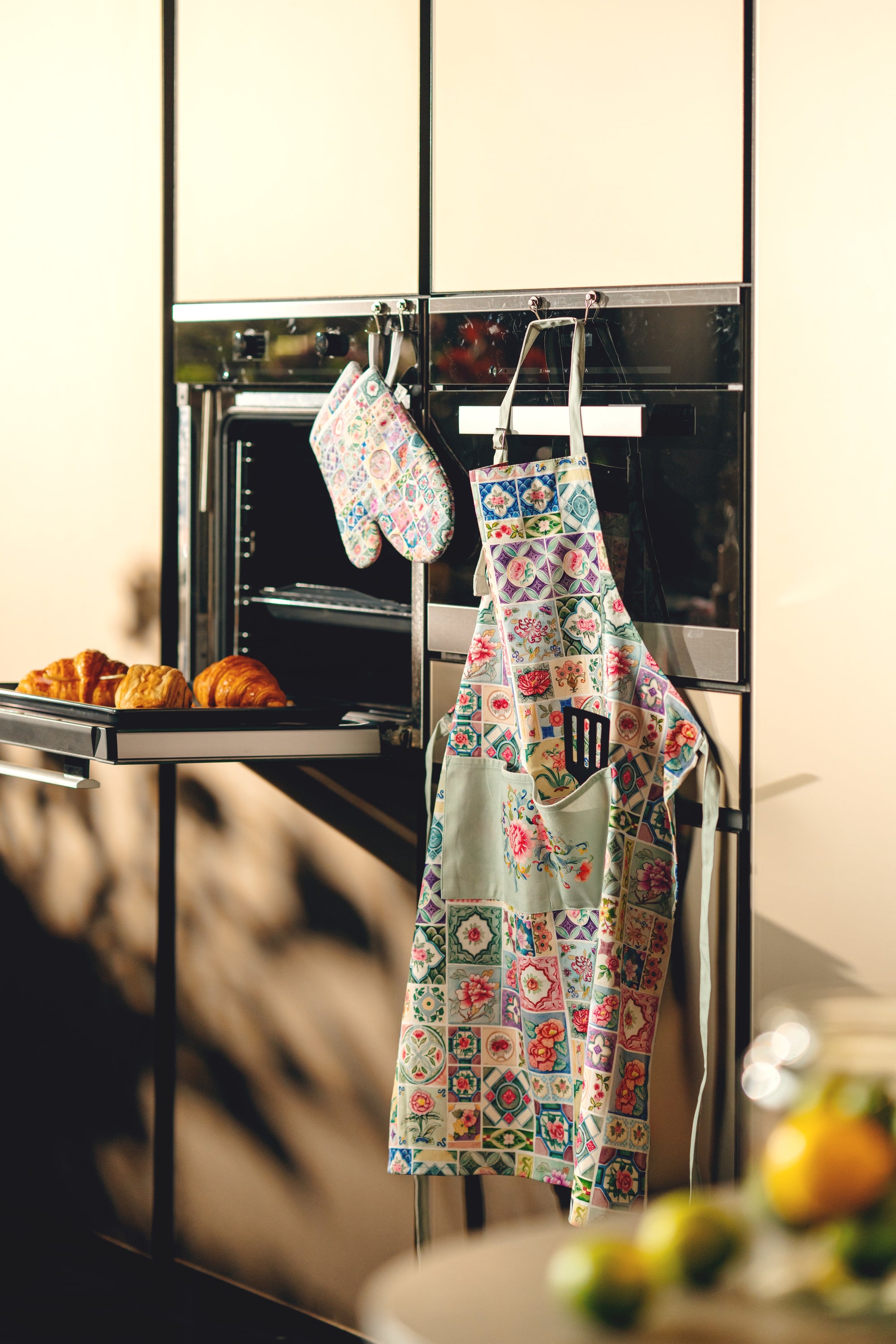 Colorful apron and oven mitts hanging on a modern kitchen appliance.