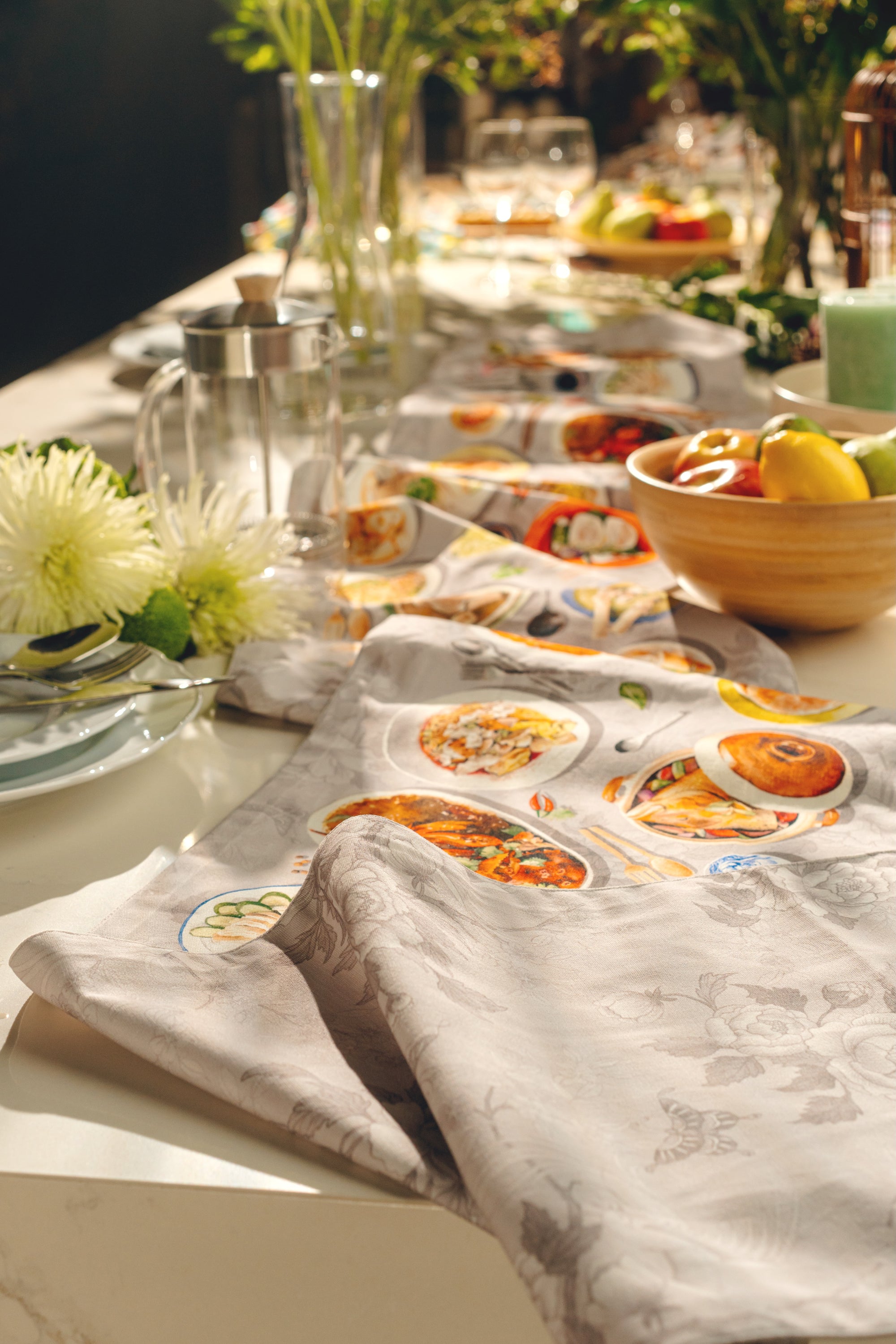 Table runner all over dining table with glassware and a bowl of fruits.