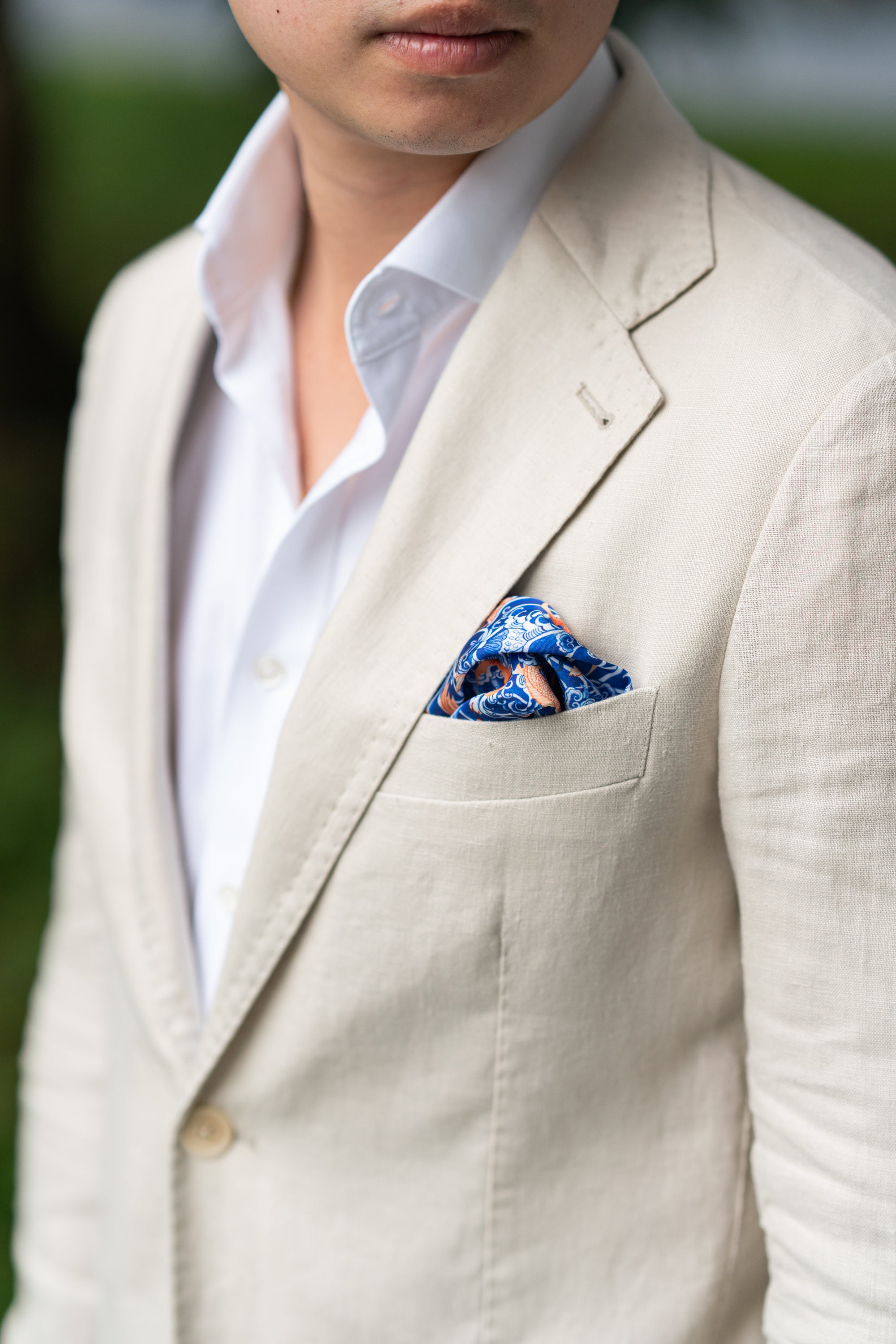 Man wearing a beige suit with a blue wave pocket square.