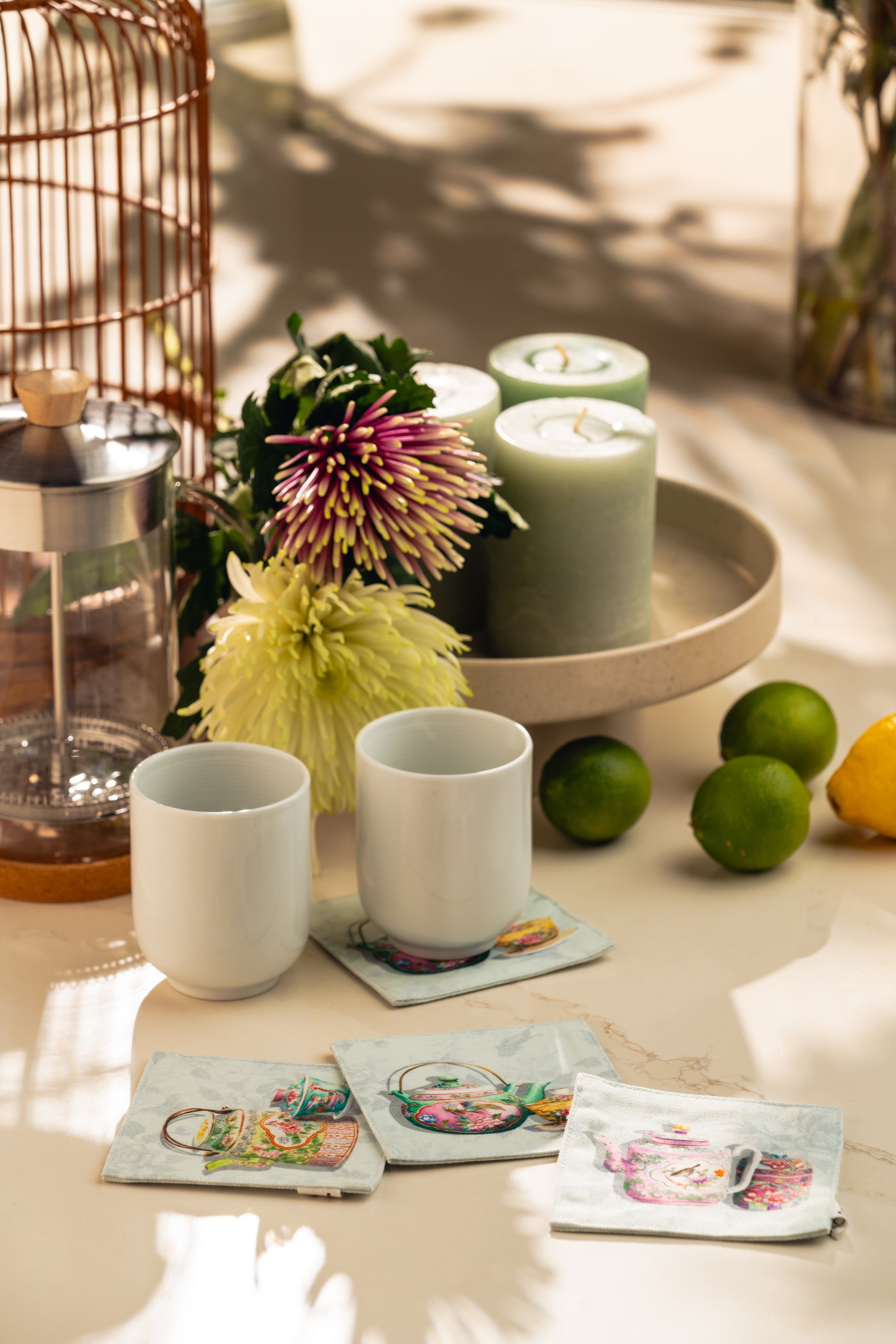 Ceramic cups, coasters with porcelain designs, candles, and decorative items on a table.