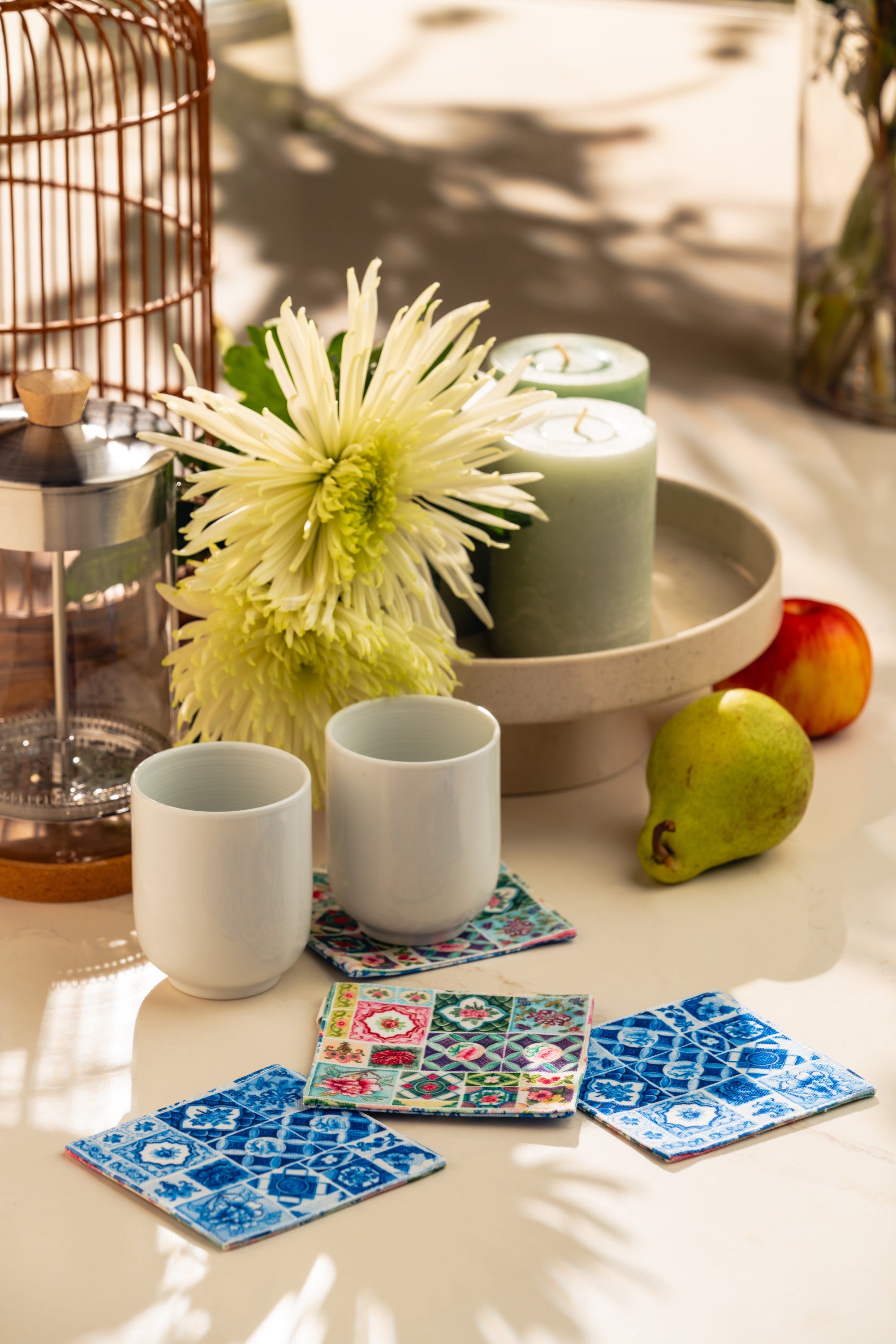 Candle holder with candles, cups, and colorful coasters on a table.